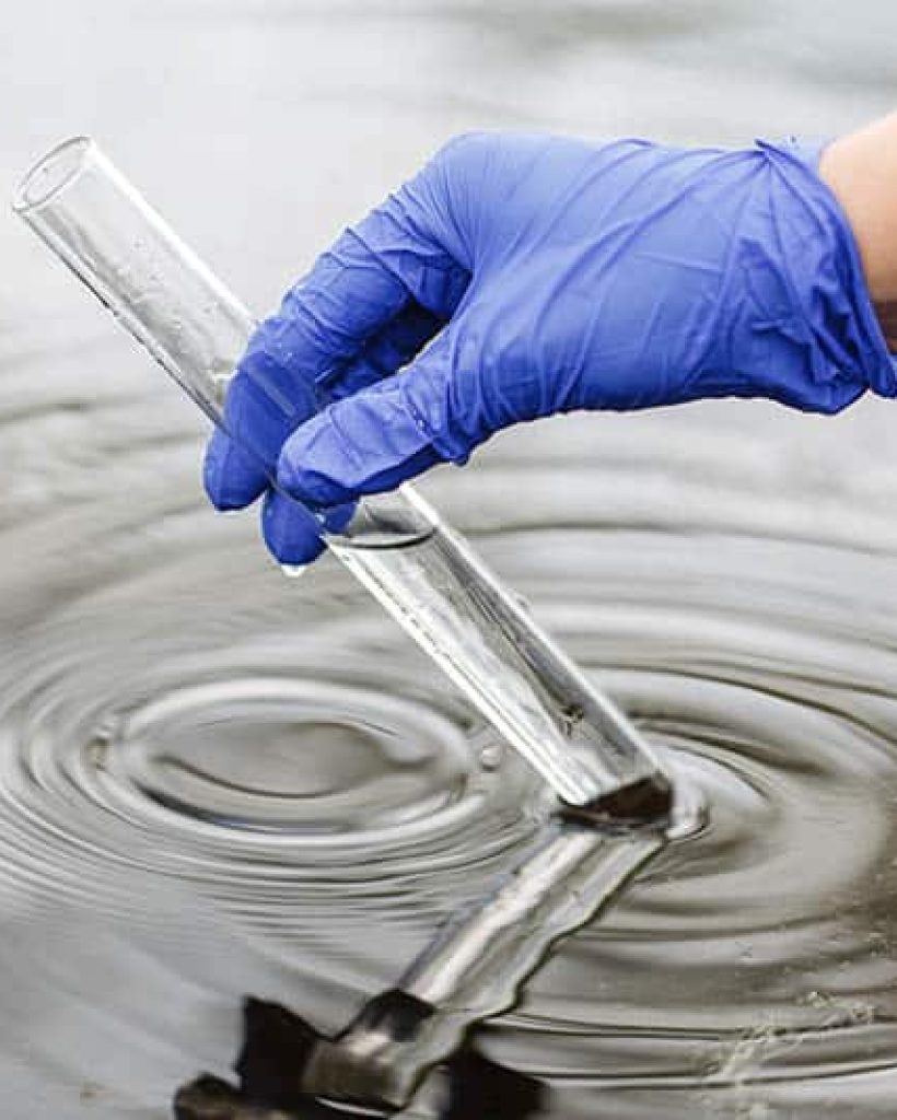 Researcher holds a test tube with water in a hand in blue glove